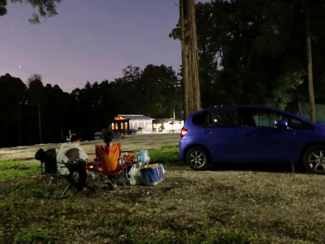 夕暮れの林で車の横に座るカーステイの2人